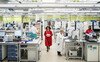 A woman in a red lab coat walks through a busy laboratory