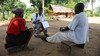 A male census field officer collects data from a woman and her son outside their home.