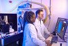 Two scientists in white lab coats looking at brain scans on a computer.