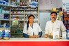 Two pharmacists stand behind a pharmacy counter in Bangalore, India.