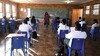 A teacher wearing a mask speaks to her students in front of the classroom.